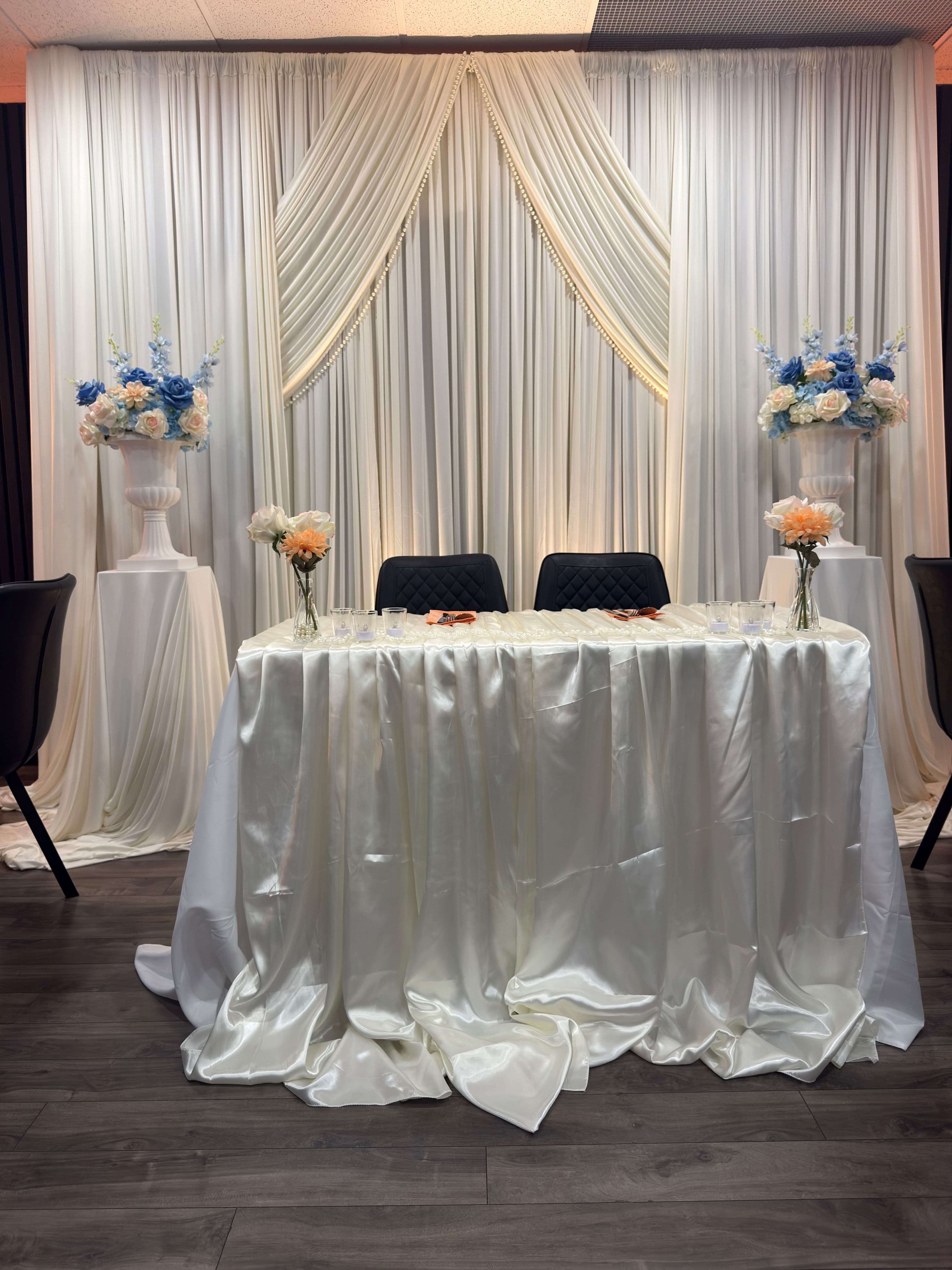 A sweetheart table framed by white draping and blue and ivory flowers at KLAS Studio